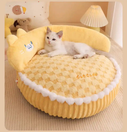 White cat lying on a yellow pet bed with cartoon face design in a cozy room.