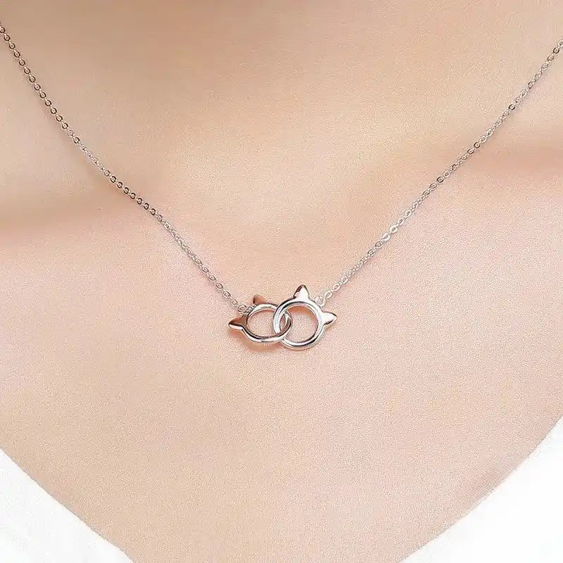 Silver necklace with a cat-shaped pendant on a person's neck against a neutral background