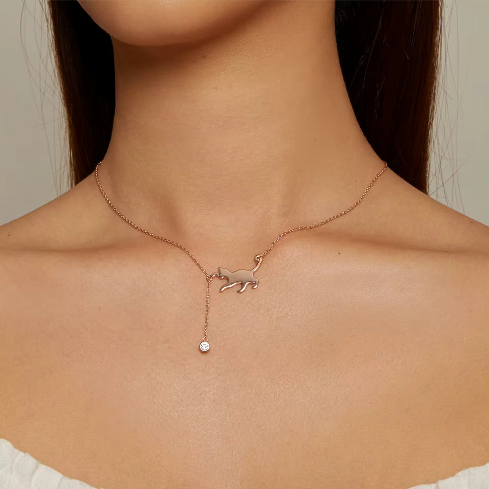 Rose gold necklace with a cat pendant on a person's neck against a neutral background