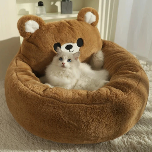 Cat lying in a brown bear-shaped cat bed on a carpeted floor.