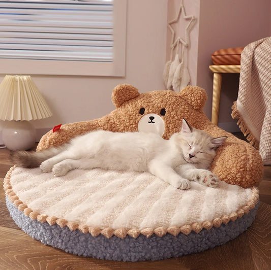 Cat lying on a round, plush pet bed with teddy bear design in a cozy room.