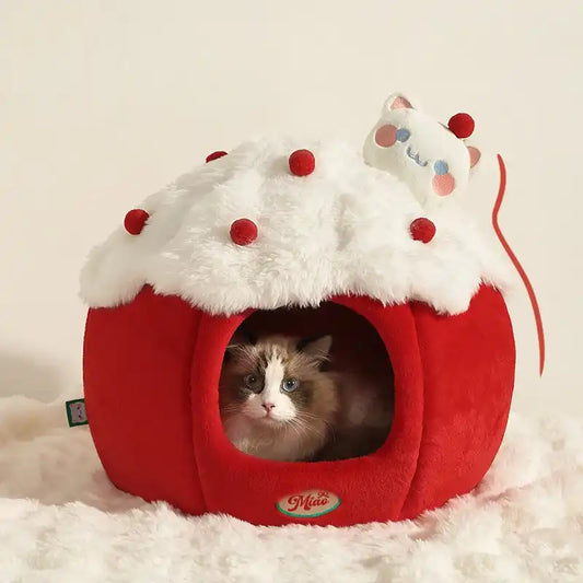 Cat peeking out from a red and white cupcake-shaped pet bed on a soft surface.